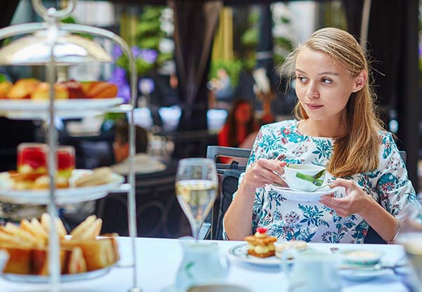 Young woman enjoying afternoon tea with selection of fancy cakes and sandwiches